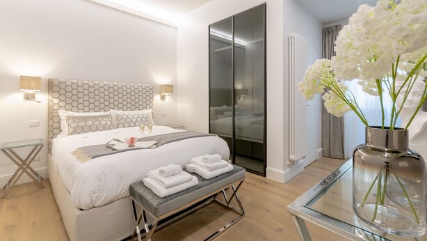 Ein modernes Schlafzimmer mit einem großen Bett, Nachttischen, einem Glastisch und einer Vase mit Blumen.