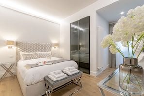 Une chambre moderne avec un grand lit, des tables de chevet, une table en verre et un vase rempli de fleurs.