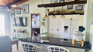 Une cuisine dotée d’un îlot central, de tabourets de bar blancs, d’un ventilateur de plafond et d’une grande fenêtre.
