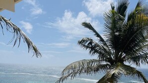 Un balcon avec une table en verre et des coussins à rayures, donnant sur une plage et l’océan.