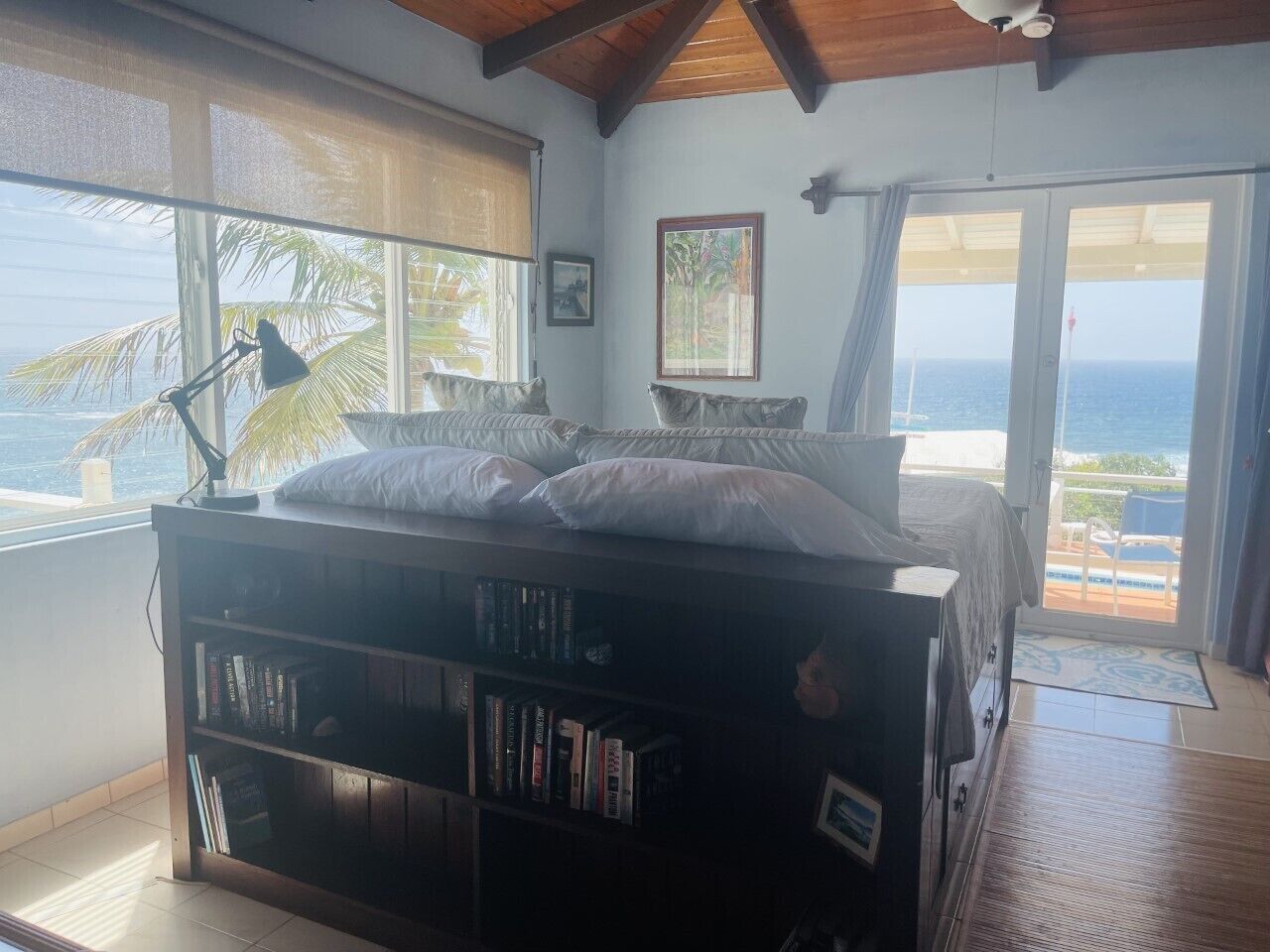 Ein Schlafzimmer mit Bett, Bücherregal, Schreibtisch und Blick auf den Ozean.