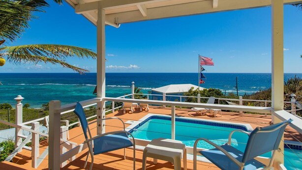 Un espace aménagé au bord de la piscine, avec vue sur l’océan, un drapeau et des chaises longues.