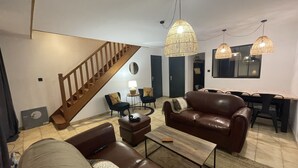 A modern living room with a staircase, leather sofas, a coffee table, and hanging pendant lights. - Charming house in the forest of Troncais (Saint-Bonnet-Tronçais)
