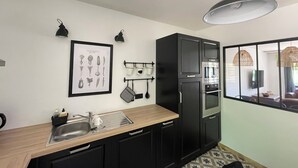 A compact kitchen with a sink, black cabinets, a microwave, and a hanging pot rack. - Charming house in the forest of Troncais (Saint-Bonnet-Tronçais)