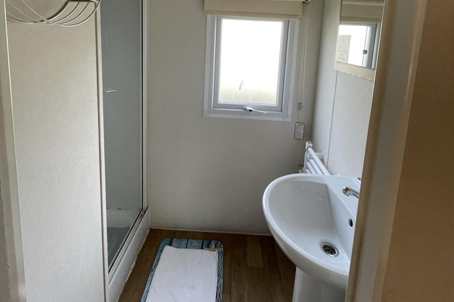 A small bathroom with a shower, a window, and a sink.