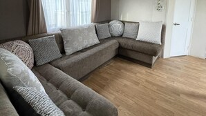 A sectional sofa with multiple cushions and a wooden floor. - Caravan - Sleeps 10 - Pet Friendly - Parking (Clacton-on-Sea)
