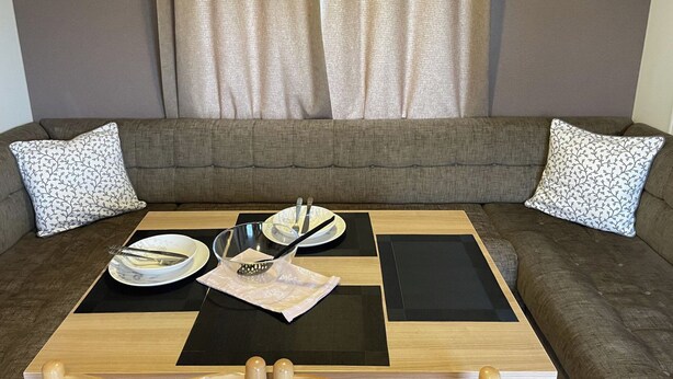 A living room with a sofa, two patterned pillows, a coffee table with plates, a strainer, and a tray. - Caravan - Sleeps 10 - Pet Friendly - Parking (Clacton-on-Sea)