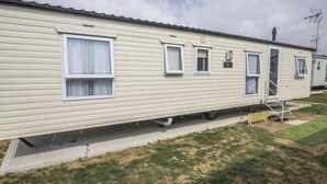A row of mobile homes with individual windows, a small porch, and a grassy yard. - Caravan - Sleeps 10 - Pet Friendly - Parking (Clacton-on-Sea)