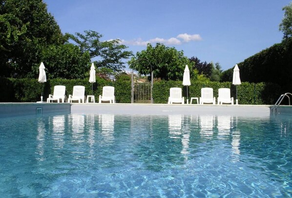 A clear swimming pool with white lounge chairs and umbrellas, surrounded by greenery.