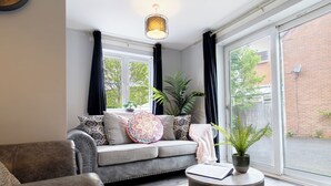 En stue med en sofa, et rundt sofabord, en potteplante og et vindue med gardiner.