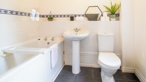 Et badeværelse med badekar, vask, toilet og et spejl over vasken.