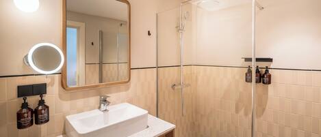A modern bathroom with a white sink, mirror, and glass shower enclosure.