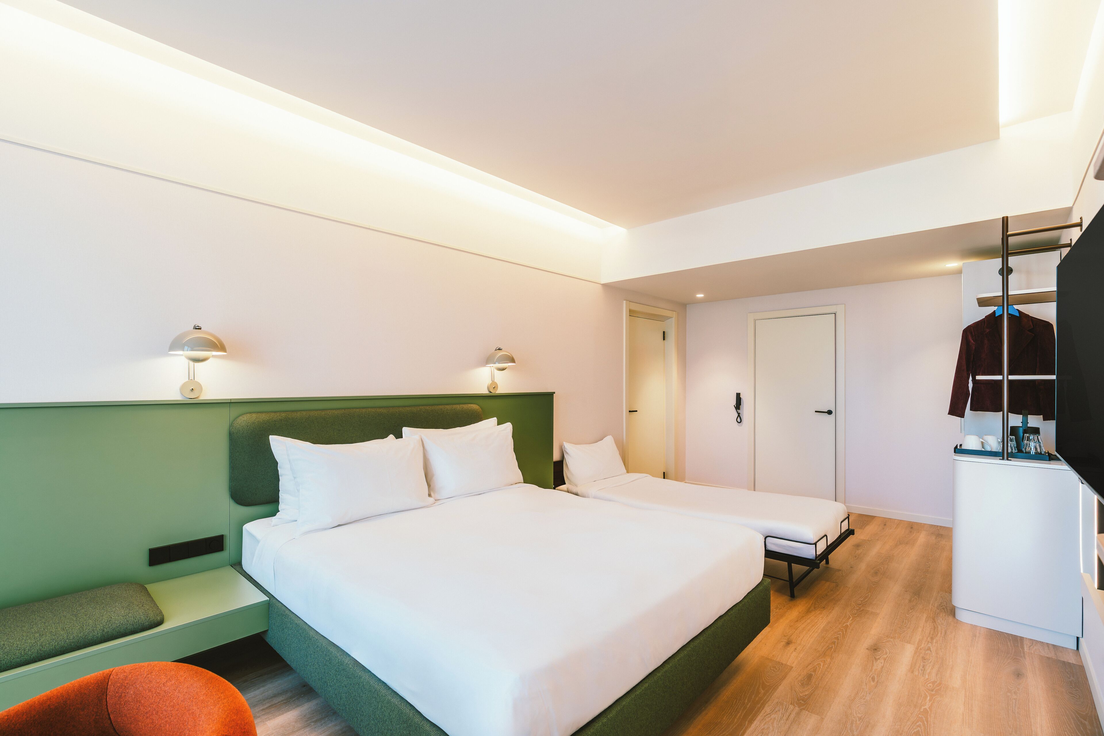 A hotel room with a large bed, bedside tables, a desk, a chair, and a coat rack.