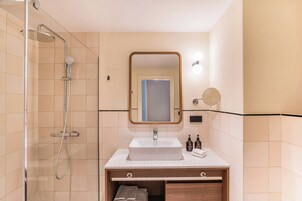 A modern bathroom with a glass shower enclosure, a white sink, a wooden vanity, and a mirror with wall-mounted lights.