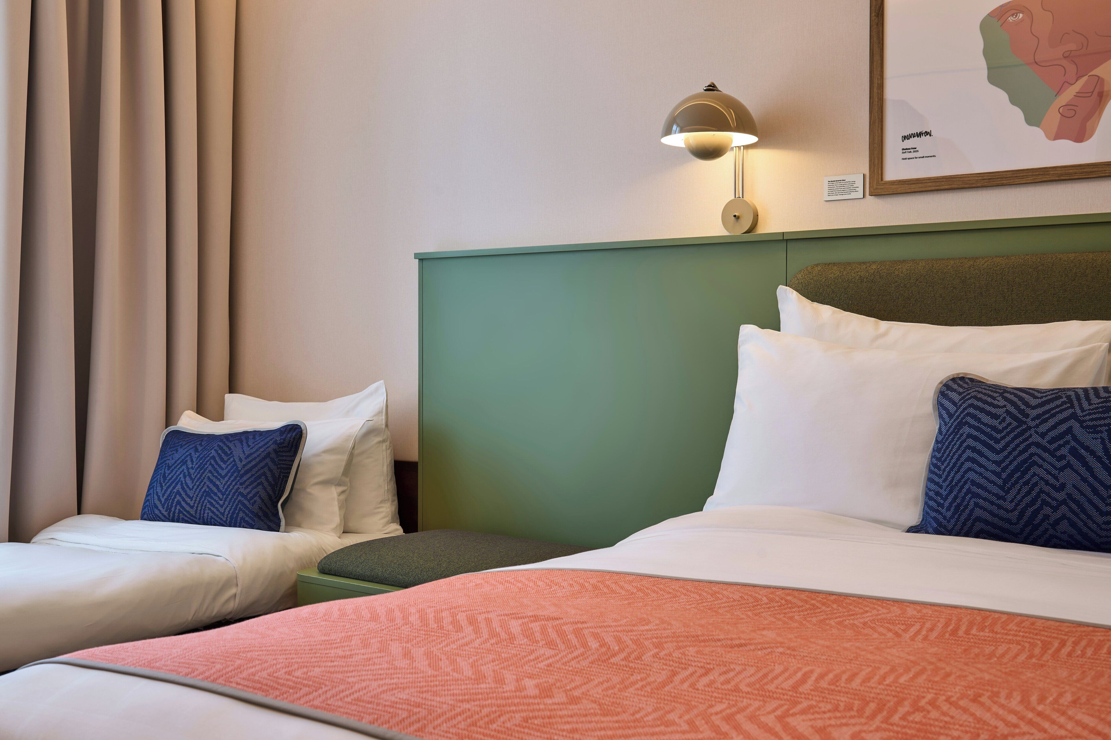 A hotel room with two beds, a green headboard, a map on the wall, and a lamp.