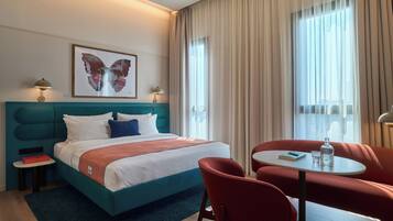 Habitació d'hotel amb un llit, una taula amb cadires, una petita taula auxiliar i una finestra amb cortines.