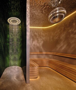 Un spa moderno con un banco curvo de madera, una fuente de agua en la pared y una lámpara colgante.