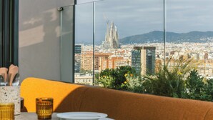 Uma área de jantar moderna com vista para a paisagem urbana, incluindo um edifício marcante com design arquitetônico único.
