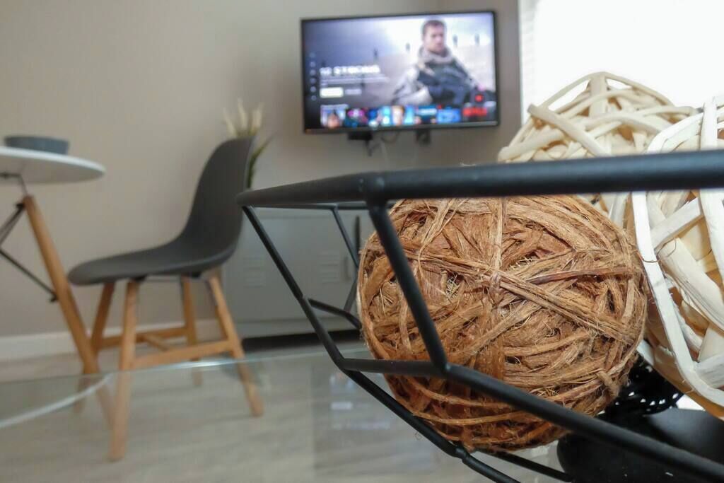 A room with a modern chair, a television displaying a person, and a decorative woven ball.