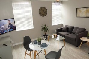 Ein modernes Wohnzimmer mit einer Couch, einem Esstisch mit Stühlen, einer Uhr und einem Fernseher, der ein Videospiel zeigt.
