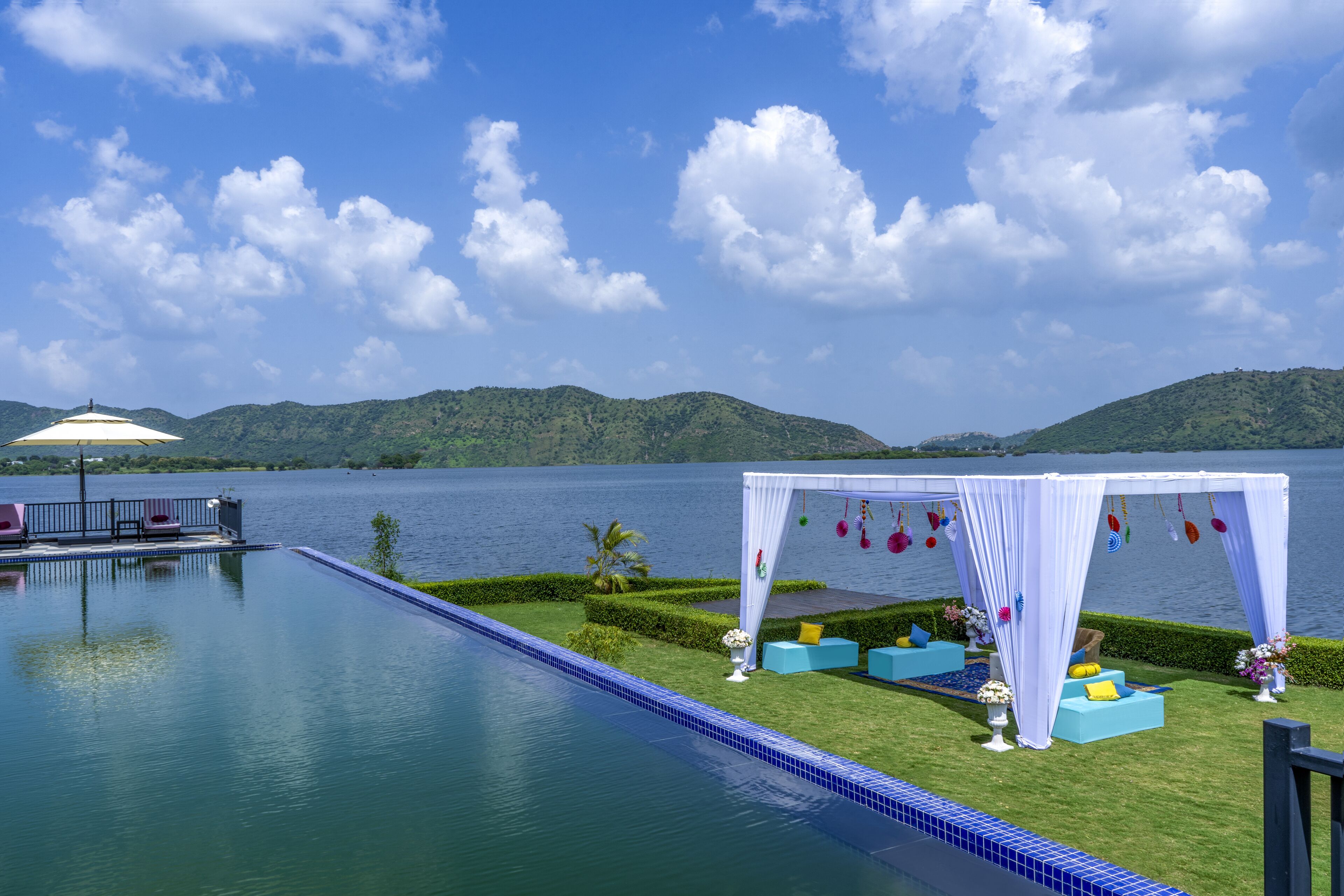 A poolside area with a white canopy, seating, and a view of a lake and mountains.
