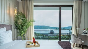 A hotel room with a bed, a tray with food and drink, a chair, a large window with a view of a lake and mountains. - Zana Lake Resort Udaipur (Udaipur)
