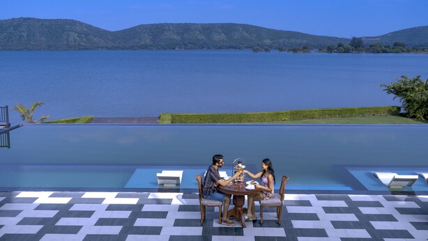 A poolside dining area with a view of a lake and hills. - Zana Lake Resort Udaipur (Udaipur)