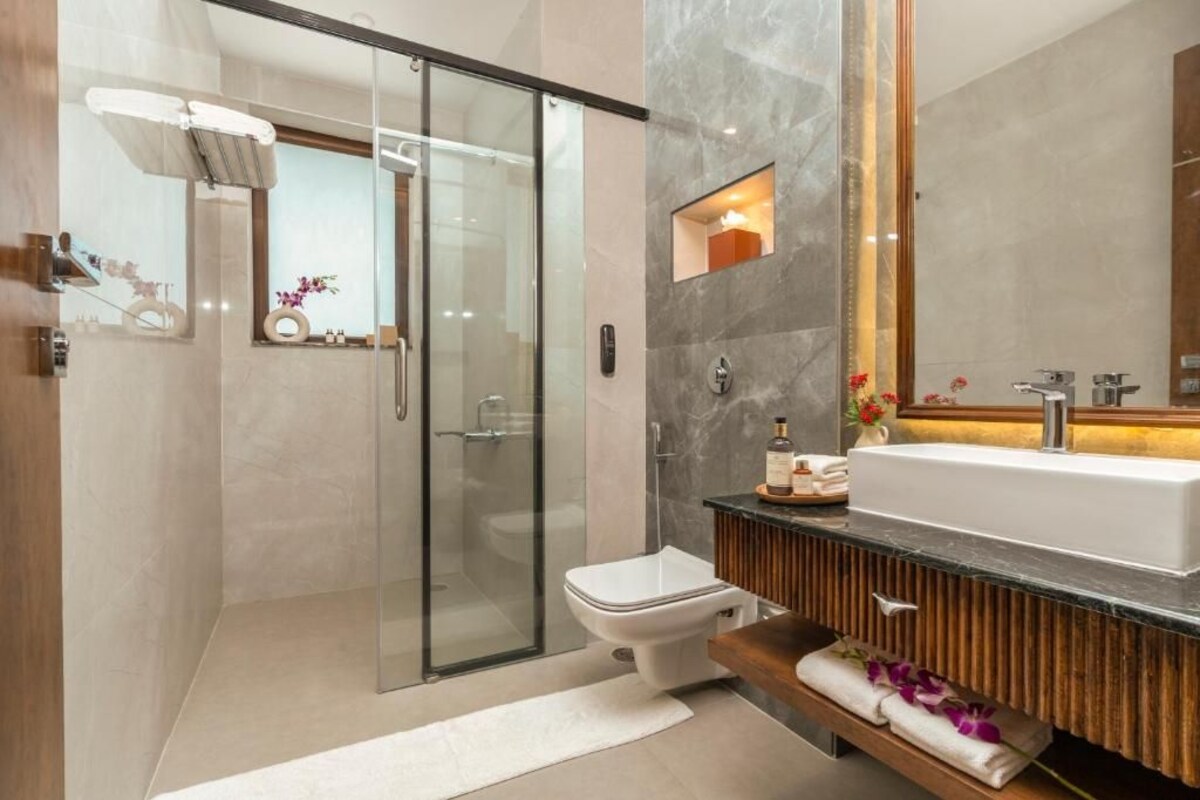 Een moderne badkamer met een glazen douchecabine, een wit toilet, een ruime wastafel en een wastafelmeubel met een spiegel.