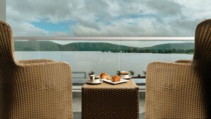 A wicker lounge chair with a table set for breakfast, overlooking a lake and mountains. - Zana Lake Resort Udaipur (Udaipur)