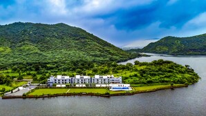 A hotel with multiple floors, situated on a lush green island surrounded by water. - Zana Lake Resort Udaipur (Udaipur)