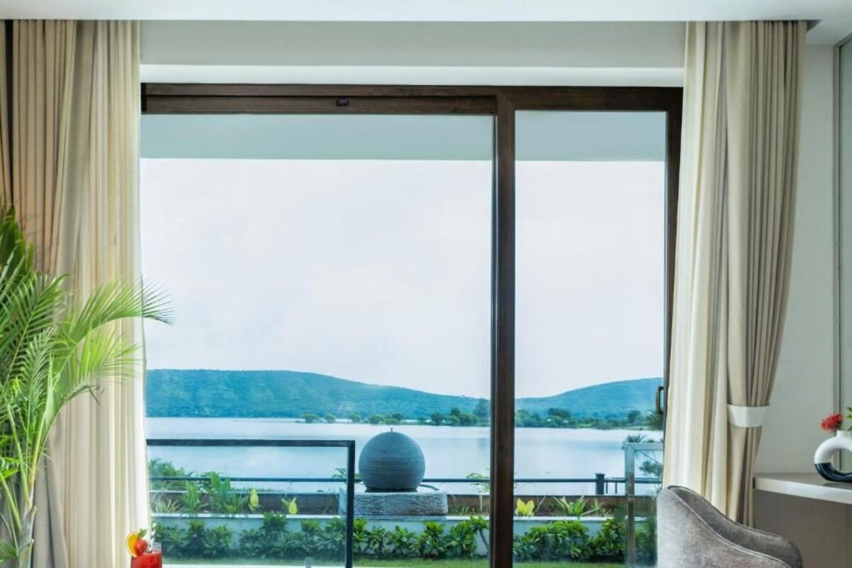 Een kamer met een grote schuifdeur die leidt naar een balkon met uitzicht op een meer en heuvels.