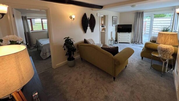 A living room with a sofa, a coffee table, a TV, and a lamp. There is a plant and a wall-mounted decoration. - Cosy Wrekin View Annexe (Eaton Constantine)