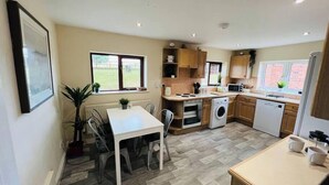 A compact kitchen with a dining area, built-in appliances, and a view of the outdoors. - Cosy Wrekin View Annexe (Eaton Constantine)