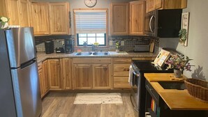 A kitchen with wooden cabinets, stainless steel appliances, a clock, and a window with blinds. - Cozy Hideaway in Denison Tx (Denison)