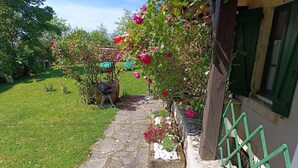 A stone pathway leading to a house with a green railing, a small garden with flowers, and a thatched structure. - ''le Cocon'' (Tracy-sur-Loire)