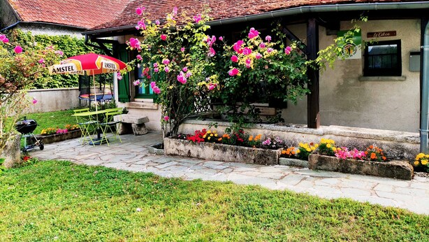A building with a tiled roof, a garden with flowering plants, a red and yellow umbrella, and a sign reading "AMSTEL." - ''le Cocon'' (Tracy-sur-Loire)
