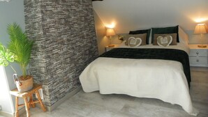 A bedroom with a stone wall, a bed with heart-shaped pillows, a nightstand with a lamp, and a potted plant. - ''le Cocon'' (Tracy-sur-Loire)