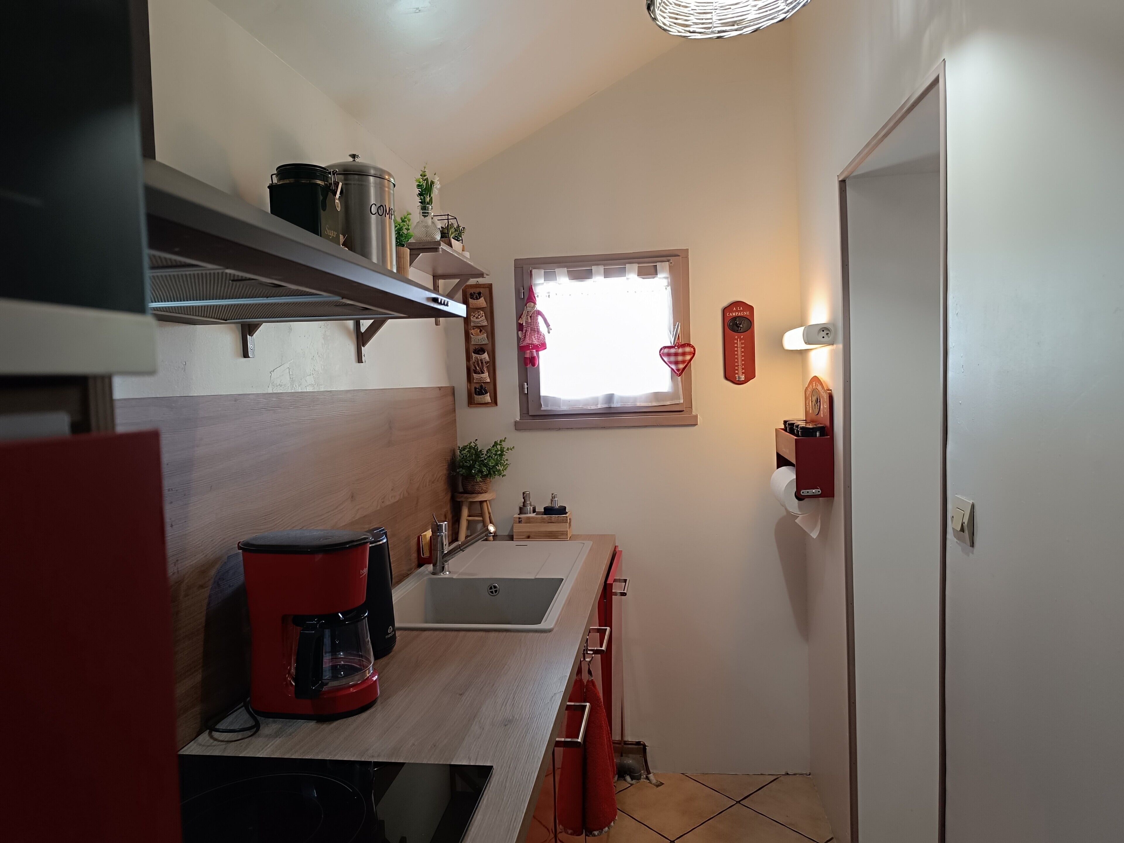 Een kleine keuken met een koffiezetapparaat, een spoelbak en een raam met gordijn.