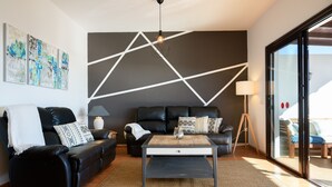 A modern living room with a black leather sofa, a wooden coffee table, and abstract wall art.