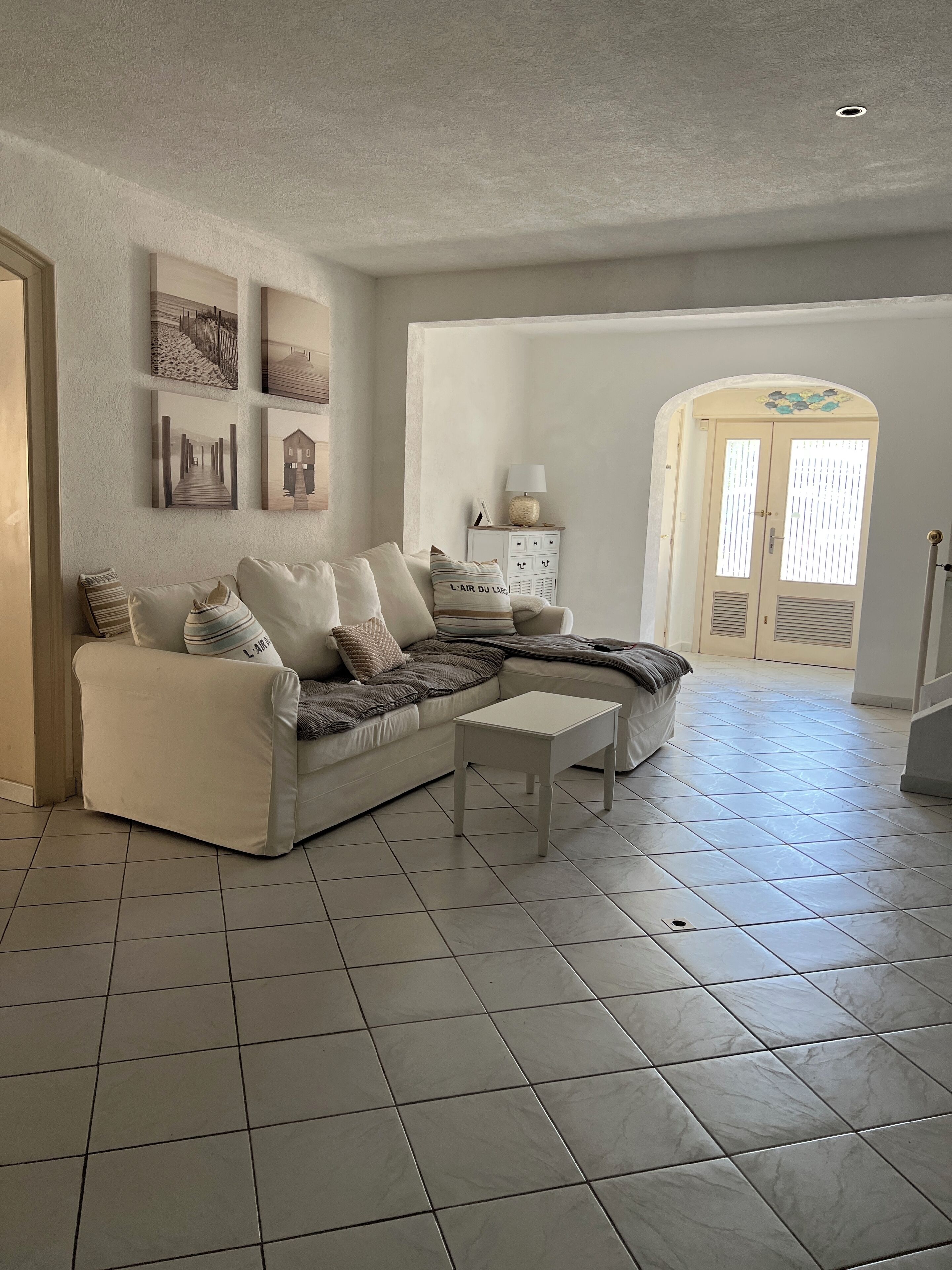 Un salon avec un canapé d’angle beige, une petite table d’appoint blanche et un meuble blanc agrémenté d’objets décoratifs.