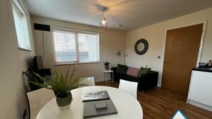 A compact living space with a round dining table, a black sofa, a small side table, a potted plant, and a ceiling light fixture.
