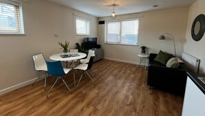 A compact living space with a dining area, a television, a small table with chairs, a sofa, and a radiator.