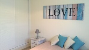 Et soveværelse med seng, puder, et natbord, en lampe og et kunstværk med ordet "LOVE".