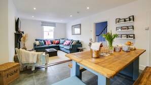A modern living room with a blue sofa, a wooden dining table, and a kitchen area with a blue countertop. - A beautiful renovated Georgian house minutes walk to Port Isaac's harbourside (Port Isaac)