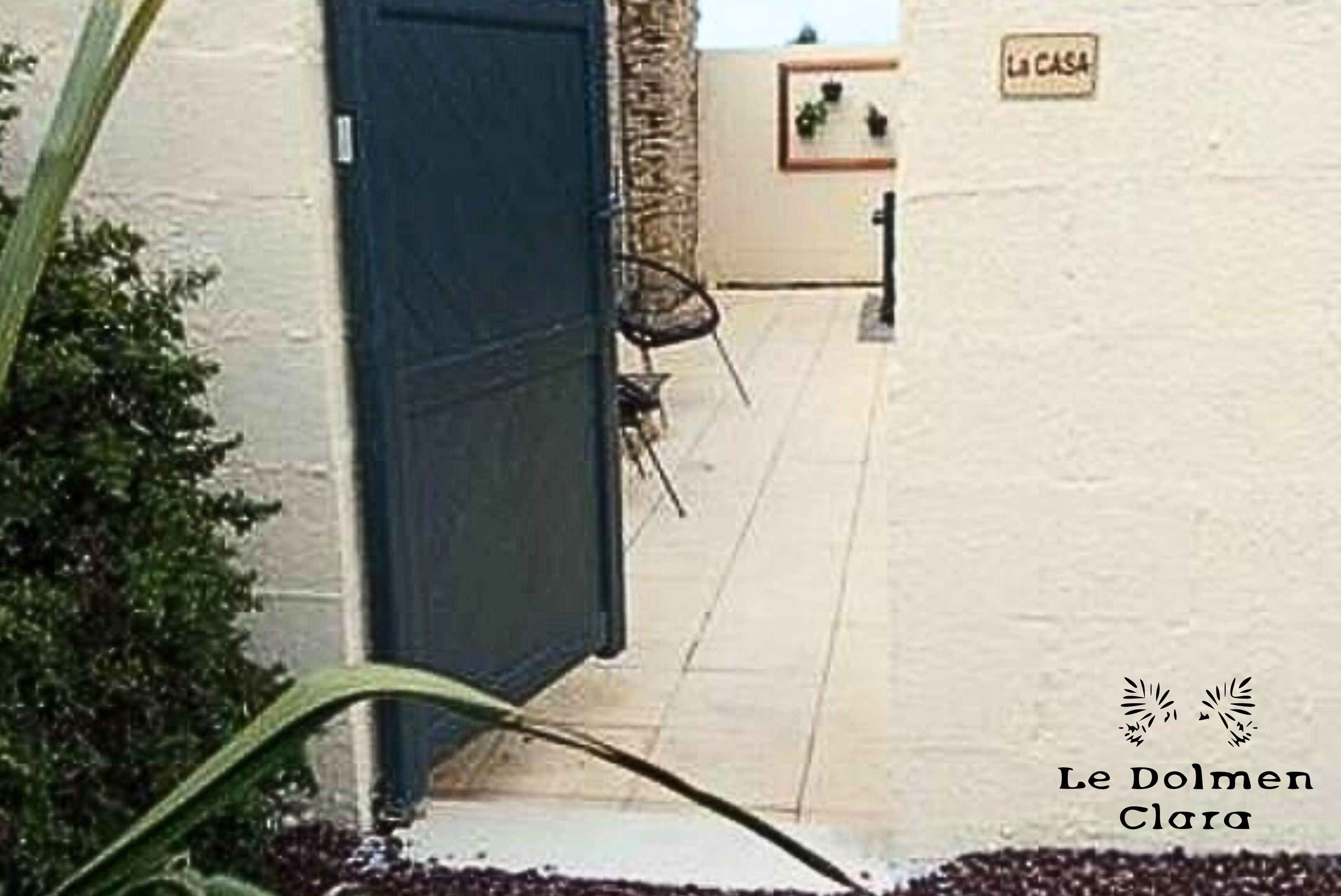 A hallway with a blue door, a sign reading "LA CASA", and some greenery.