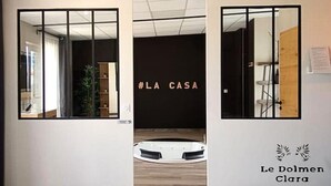 Vista del interior de un moderno vestíbulo de hotel con puertas de vidrio, un mostrador de recepción de madera y una pared con el hashtag #LA CASA.