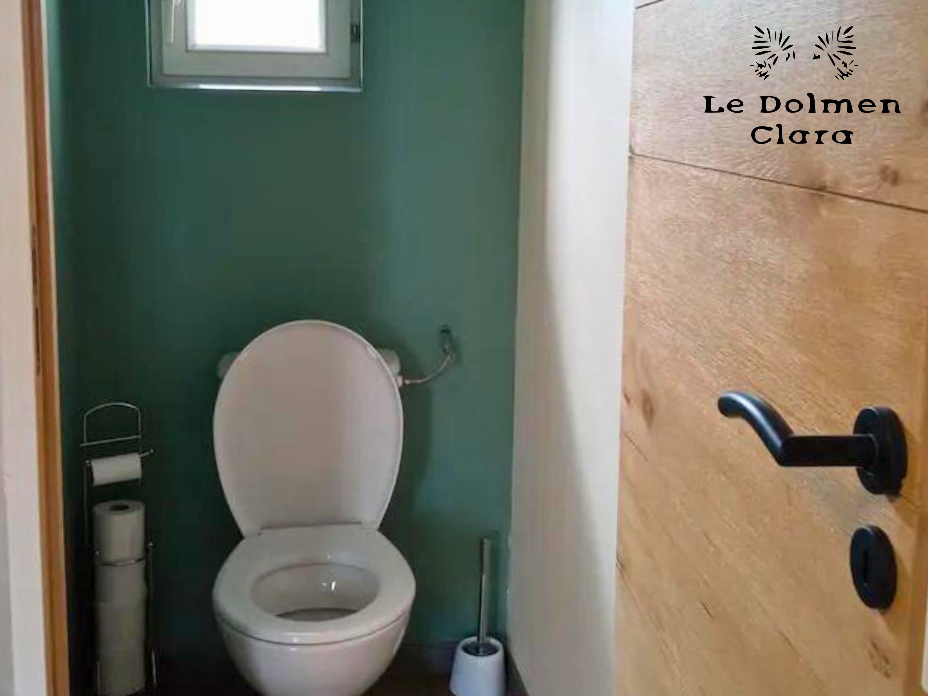 Une petite salle de bain comprenant des toilettes, un porte-rouleau de papier toilette et une fenêtre située au-dessus des toilettes.
