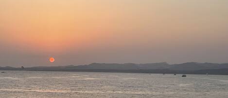 A sunset over a calm body of water with distant mountains and a pier in the foreground.