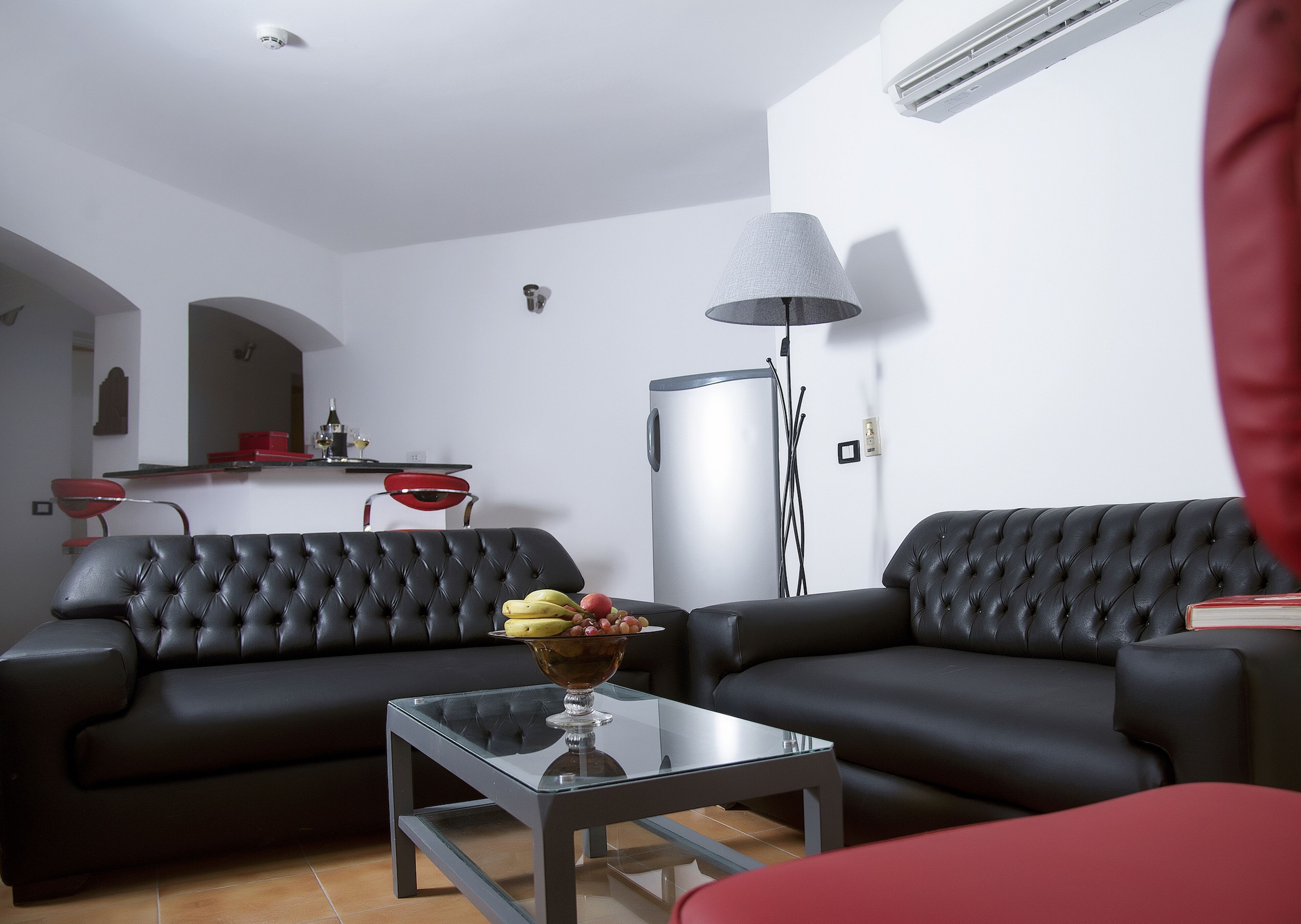 A modern living room with two black leather sofas, a glass coffee table, and a floor lamp.
