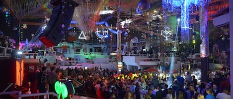 A crowded indoor event with a large audience, various light decorations, and a stage area.